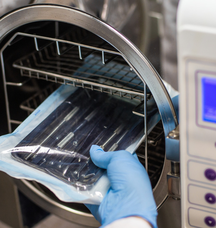 A gloved technician inserts surgical tools to be sterilized.